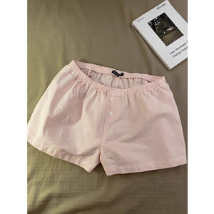 Pink striped shorts with elastic waist and front button laid flat on a bed next to a book