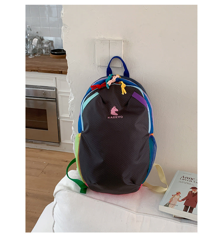 Black color block backpack on a white bed, rainbow contrast trim and two stretch mesh side pockets