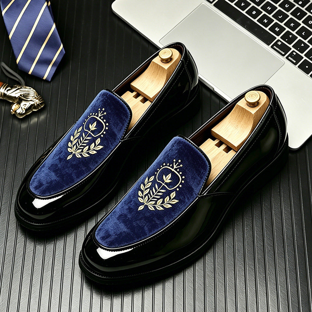 Glossy black loafers with a blue velvet vamp and an embroidered laurel crest on a desk with a tie, size 46 option
