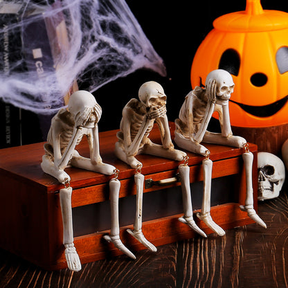 Three resin skeleton shelf sitters in see hear and speak no evil poses beside a pumpkin