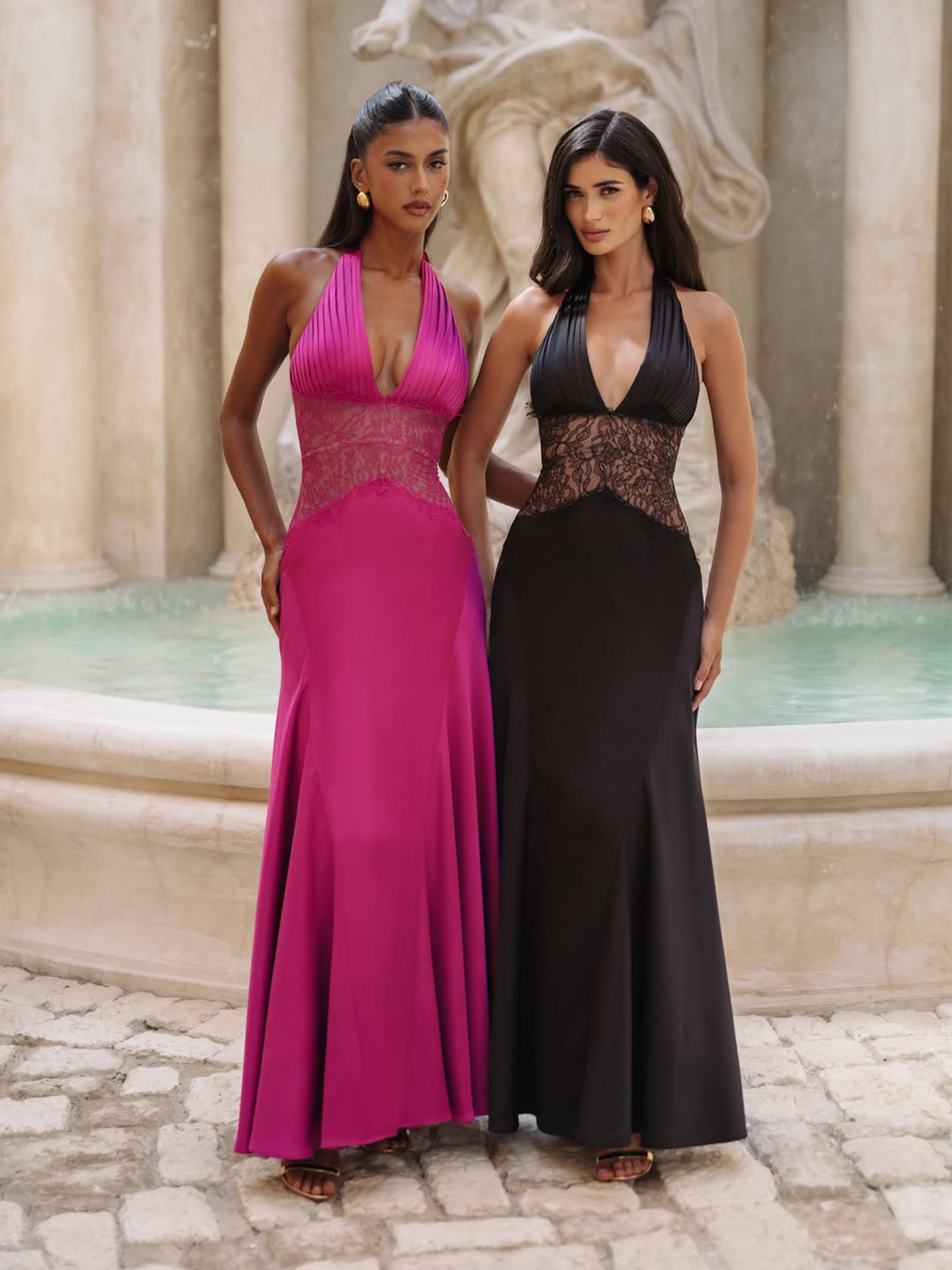 Two models in a halter maxi gown, one magenta and one black, front view by a fountain