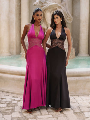 Two models in a halter maxi gown, one magenta and one black, front view by a fountain