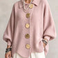Woman in a light pink loose knit top with a collar and large gold tone buttons, front view