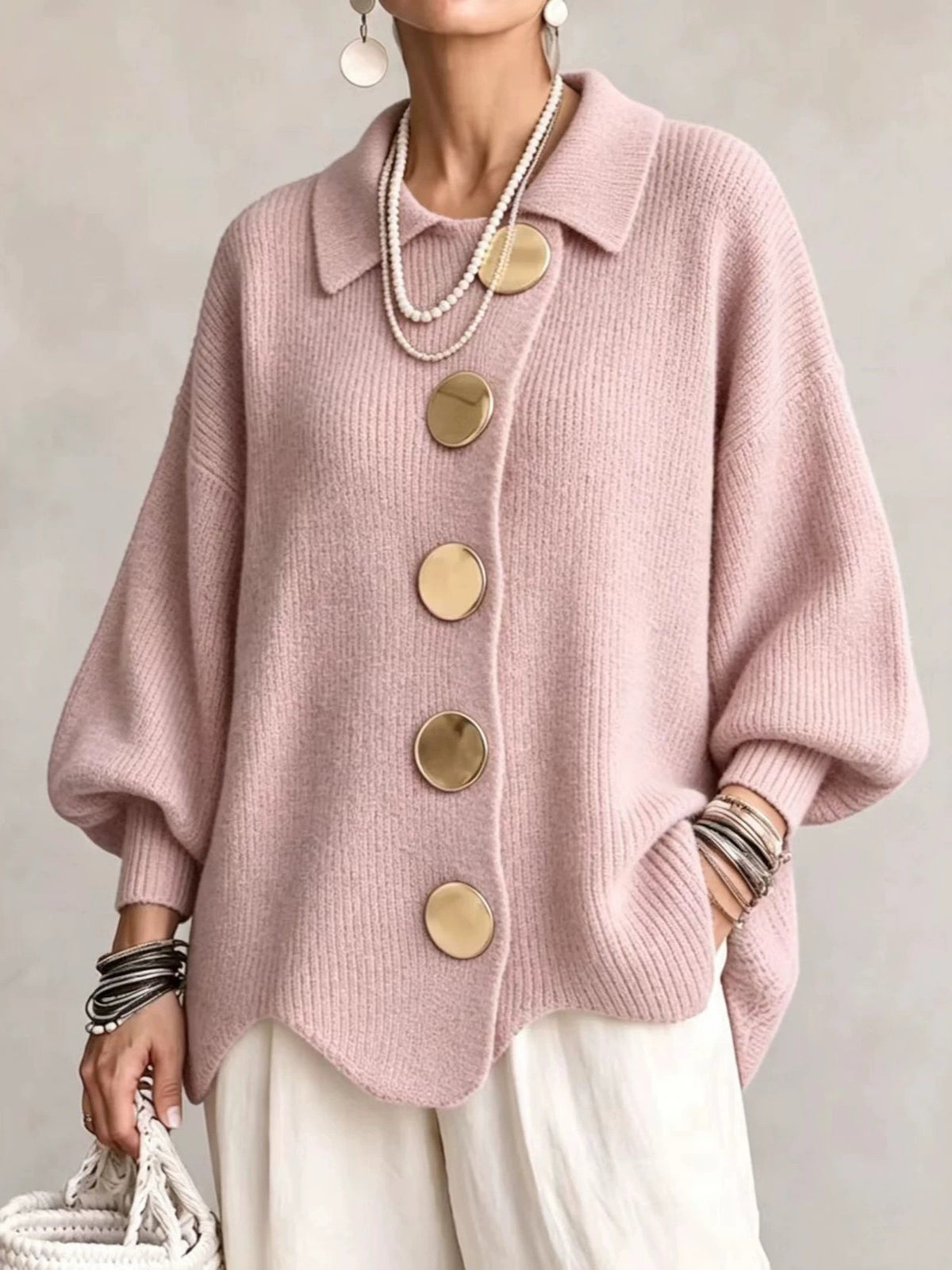 Woman in a light pink loose knit top with a collar and large gold tone buttons, front view