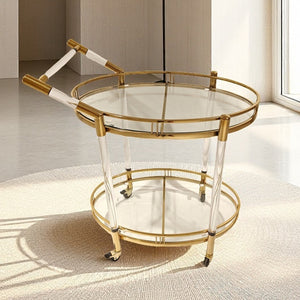 Round gold finish serving cart with glass tiers and wheels on a rug in a bright room
