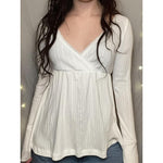 Woman in a white long sleeve crossover V neck babydoll top with lace edging and a ribbed texture, front view