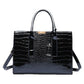 Black glossy croc pattern handbag with two top handles, buckled tab and shoulder strap, front view