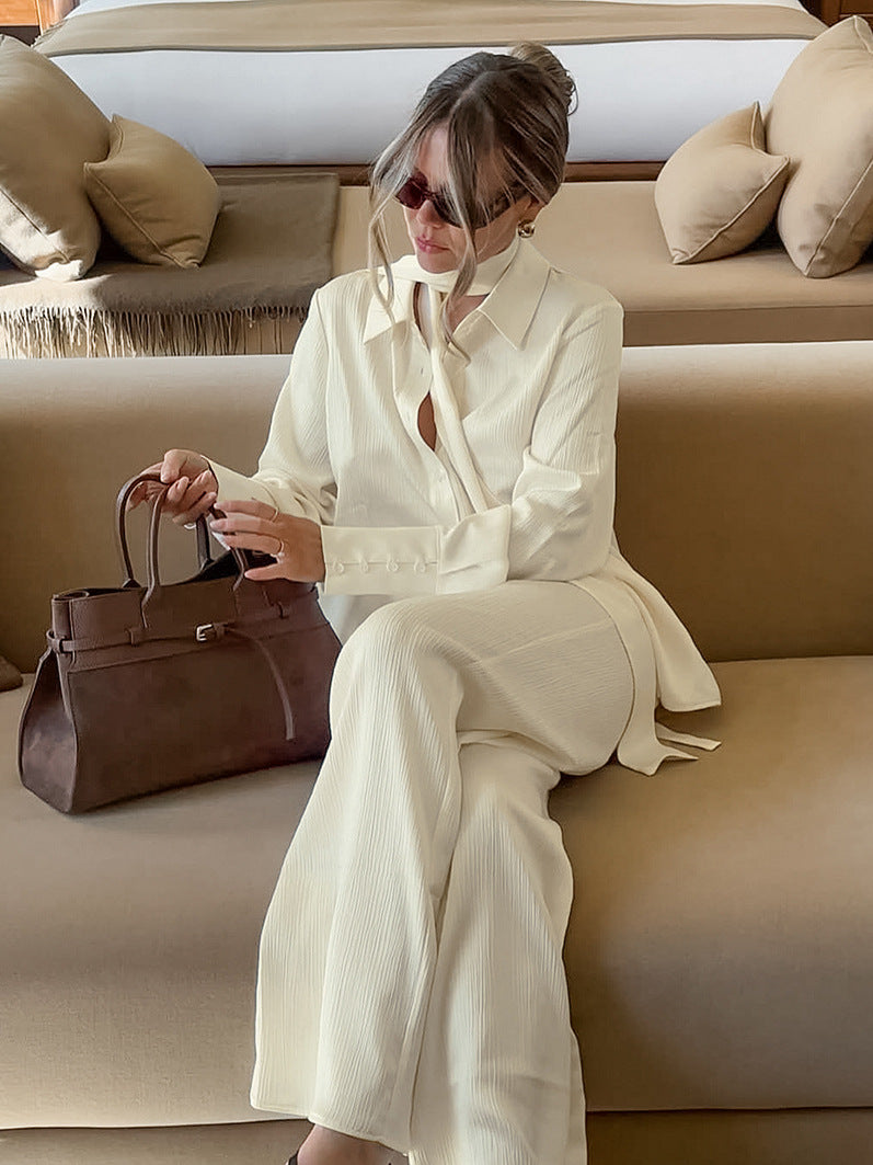 Woman in a loose buttercream long sleeve shirt and wide leg trousers two piece set, seated with a handbag