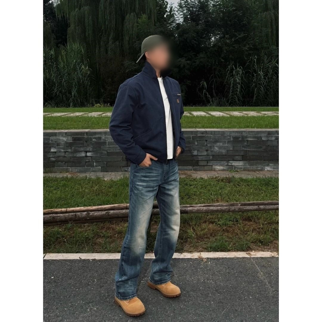 Man in a navy blue cotton jacket with a turn down collar standing on grass beside a paved path