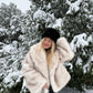 Cream vegan fur short jacket with shawl collar worn in the snow with a black hat