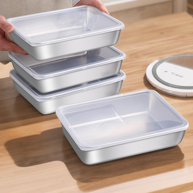 Four shallow stainless steel food trays with clear snap on lids on a wooden table