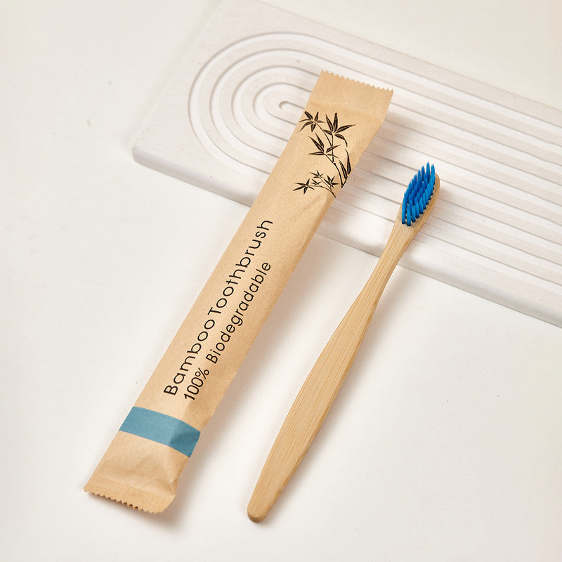 Bamboo toothbrush with colored bristles beside its kraft paper packaging