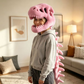 Pink plush dinosaur skeleton head mask worn from the side with the spine down the back