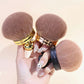 Three mushroom head brushes in gold, rose gold and black handles held in one hand