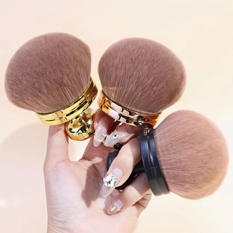 Three mushroom head brushes in gold, rose gold and black handles held in one hand