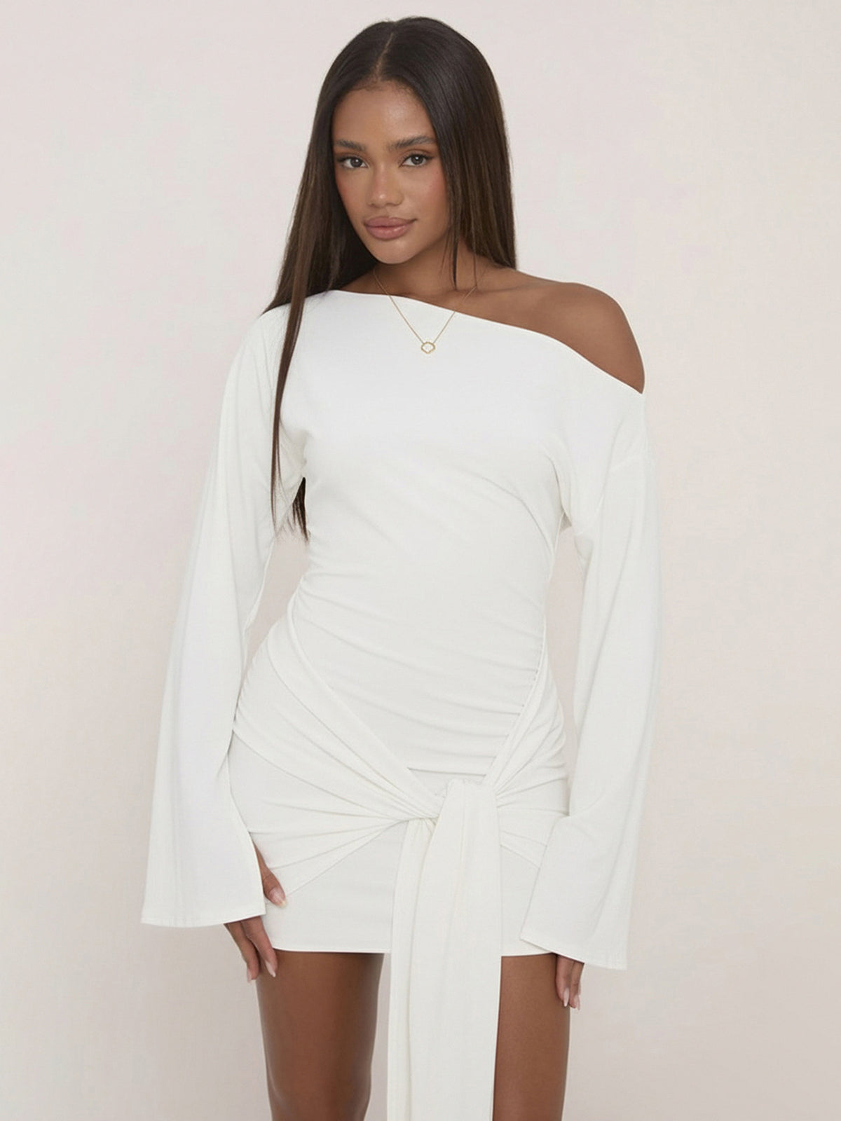 Woman in a white one shoulder bodycon mini dress with wide bell sleeves and a knotted drape at the hip, front view
