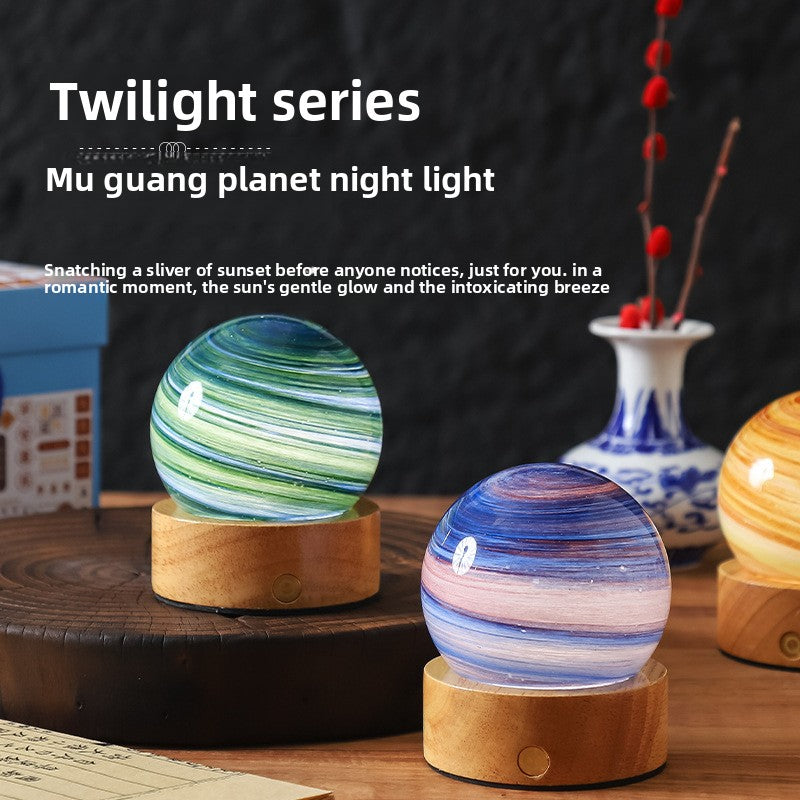 Two glass planet night lights on round wooden bases on a dark table beside a blue and white vase