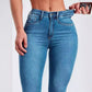 Close view of the waistband, zip fly and front pocket of denim blue high rise jeans