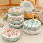 Several round bohemian print floor cushions stacked and leaning in a living room beside a cane cabinet and chair