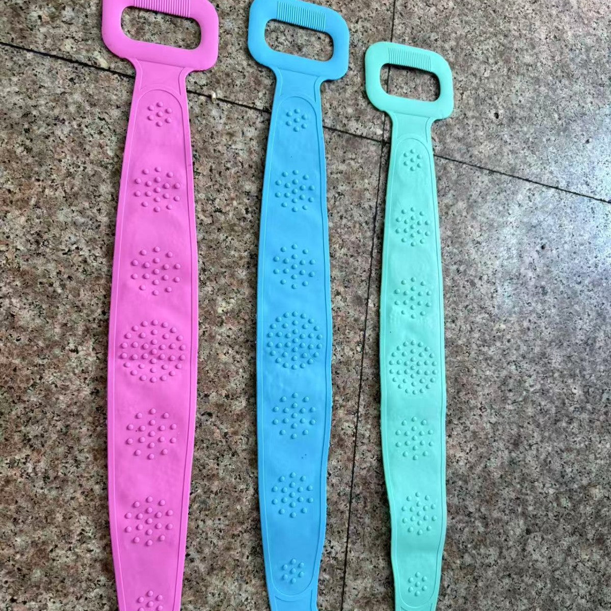 Three silicone back scrubber straps showing the raised massage nodule side in pink, blue and green