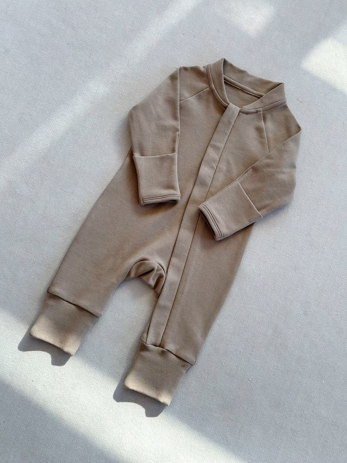Milk Tea zip front baby romper laid flat on a gray floor, image of the 80 cm, 12 to 18 months size option