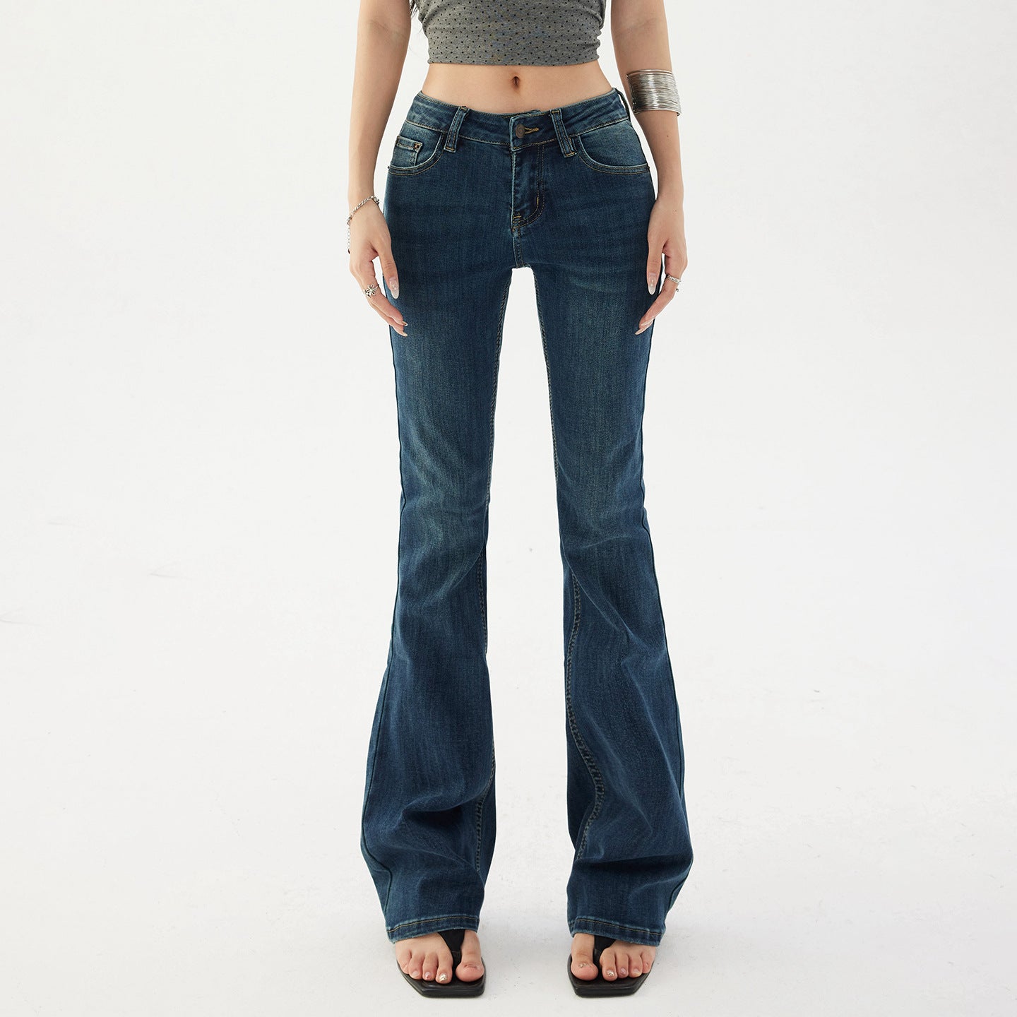 Close waist view of low rise dark denim jeans showing the button, zip fly and five pocket front