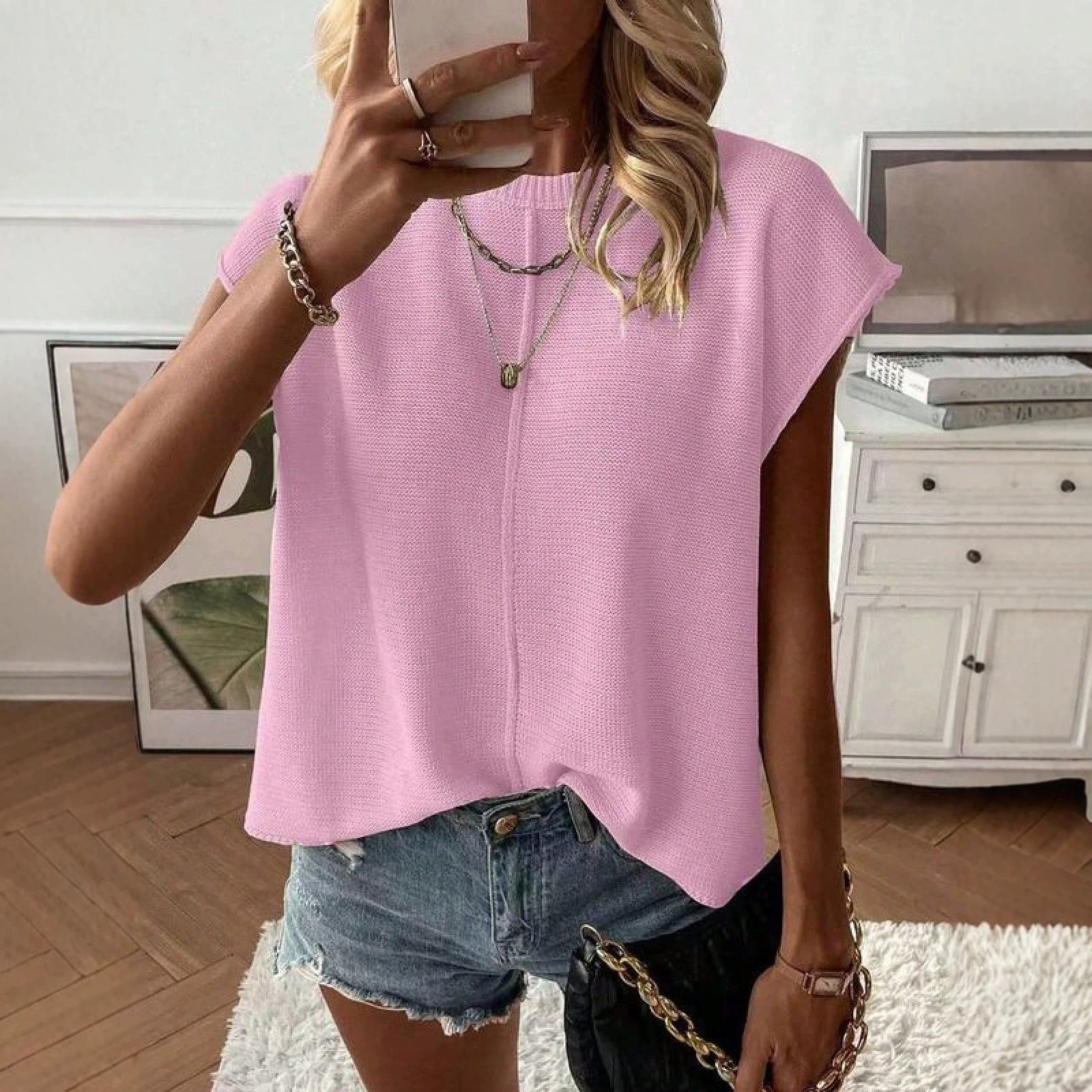 Woman wearing a pink round neck cap sleeve knit top with a relaxed drape and denim shorts
