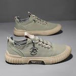 Pair of green lace up canvas sneakers with a beige ribbed sole on a gray backdrop, one shoe seen from above