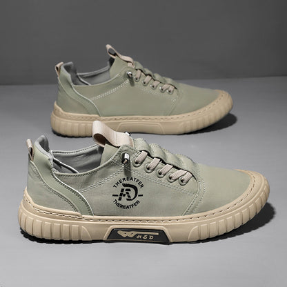 Pair of green lace up canvas sneakers with a beige ribbed sole on a gray backdrop, one shoe seen from above