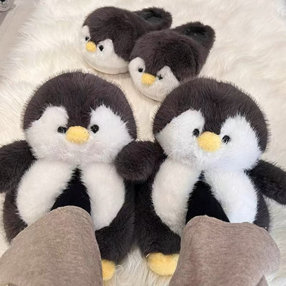 Dark gray plush penguin slippers with yellow beaks and black eyes, two pairs on a white fluffy rug, one pair worn