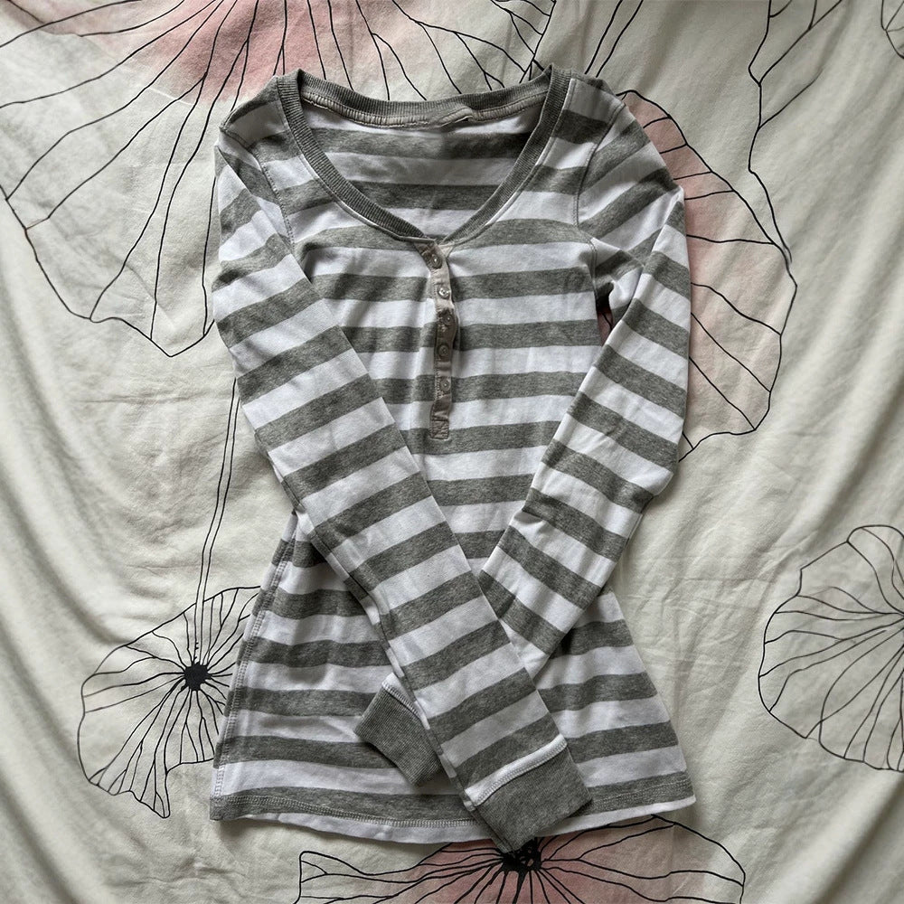 Gray and white striped henley top laid flat on a floral cloth showing the ribbed neckline and button placket