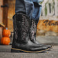 Pair of black cowboy style pull-on boots with contrast shaft embroidery outdoors