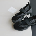Pair of black platform Mary Jane style shoes with a wide strap and elastic cords on a grey and black surface