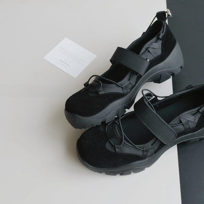 Pair of black platform Mary Jane style shoes with a wide strap and elastic cords on a grey and black surface
