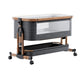 Gray fabric baby crib with a wood grain frame, wheels, mesh side window and storage basket on a white background