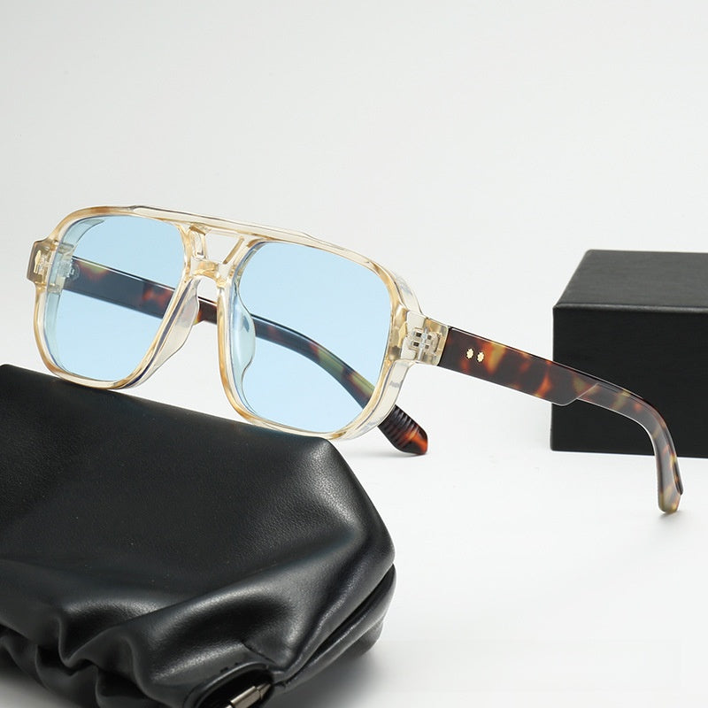 Square double bridge sunglasses with a clear yellow frame and blue lenses beside a box