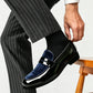 Man in pinstripe trousers putting on a glossy black loafer with a navy velvet vamp and a penny strap