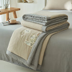 Folded cream and gray reversible double gauze summer quilt stacked on a made bed