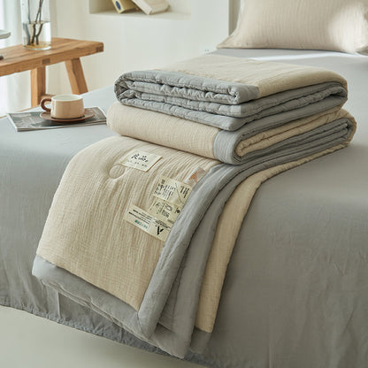 Folded cream and gray reversible double gauze summer quilt stacked on a made bed