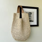 Beige crocheted paper straw shoulder bag hung on a pale wall, tan straps looped over the hook