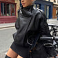 Woman in sunglasses by a shopfront in a black oversized PU leather moto jacket with a stand collar