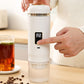 Finger pressing the power button on a white portable espresso maker with digital screen