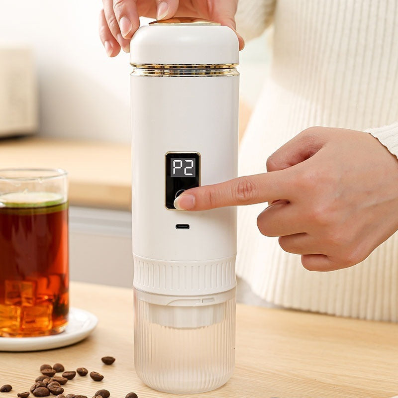 Finger pressing the power button on a white portable espresso maker with digital screen