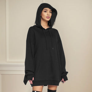 Woman in a black oversized drawstring hoodie with a front pouch pocket and long fingerless cuffs on a beige wall