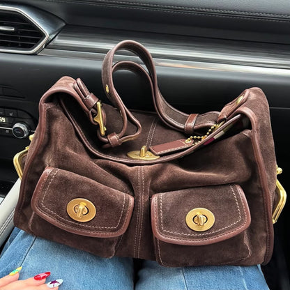 Brown suede hobo bag with a flap and two front twist lock pockets resting on a lap in a car