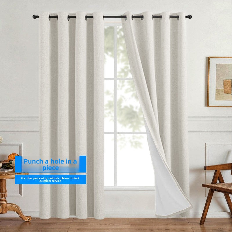 Linen look polyester blackout grommet curtain panel with white thermal backing drawn across a sunlit room frame
