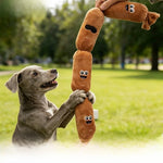 Gray dog standing on its hind legs pawing a four section plush sausage toy held up on a green lawn