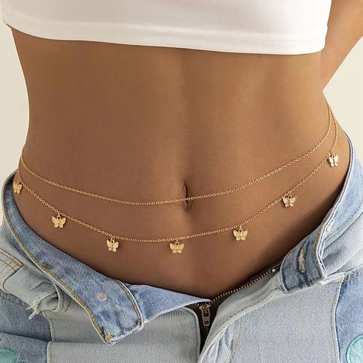 Doubled gold tone waist chain hung with small butterfly charms, worn low over open denim
