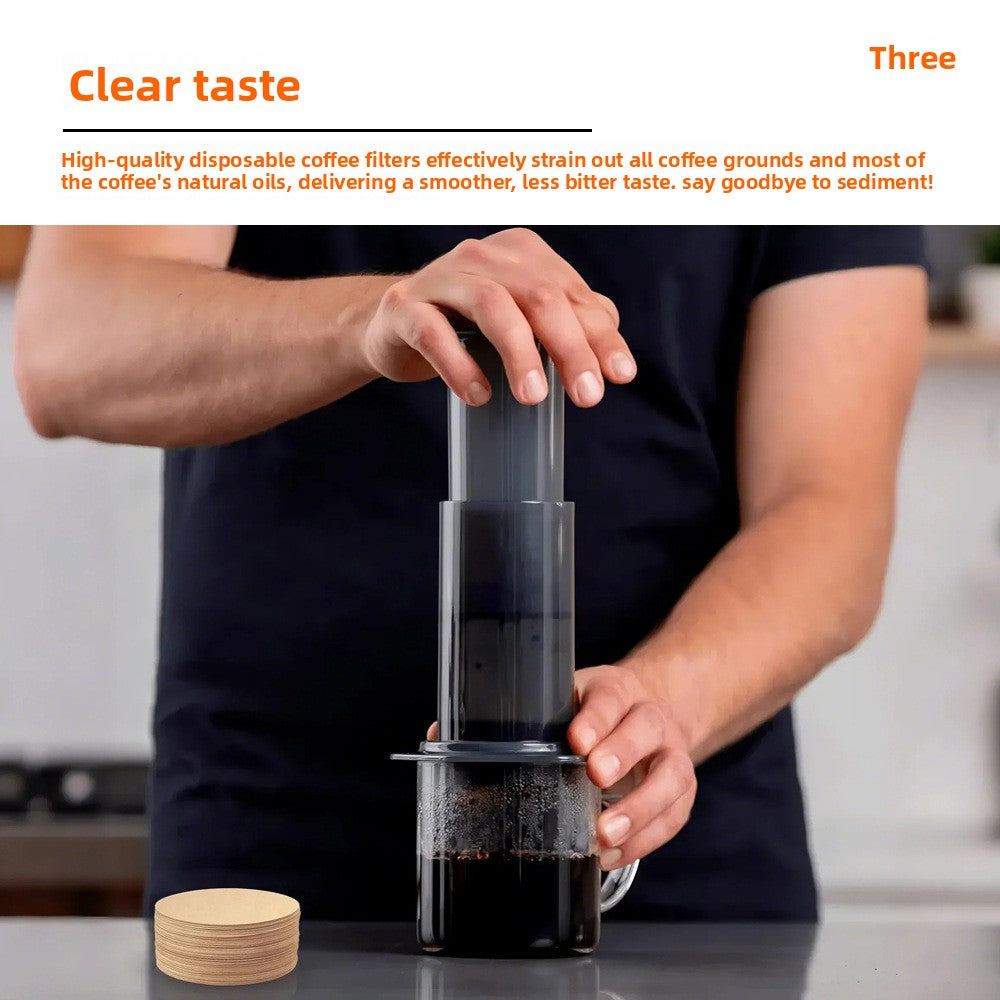 Person pressing an AeroPress style coffee maker into a glass with paper filters nearby