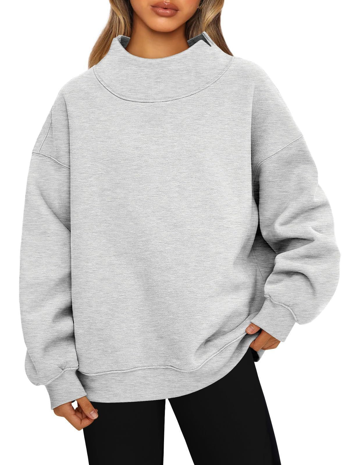 Woman in a light gray mock neck sweatshirt with dropped shoulders and ribbed cuffs, hands resting at the waist